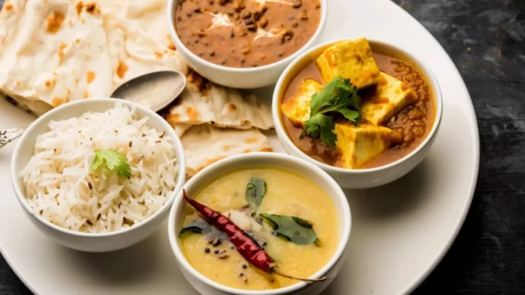 punjabi veg thali containing rice naan dal makhni shahi paneer and kadhi pakoda